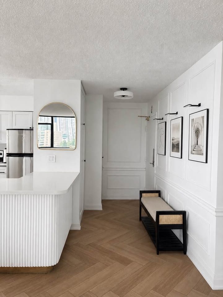 Condo entry with white picture-frame wall moulding, herringbone floors, an arched brass mirror and a fluted kitchen island