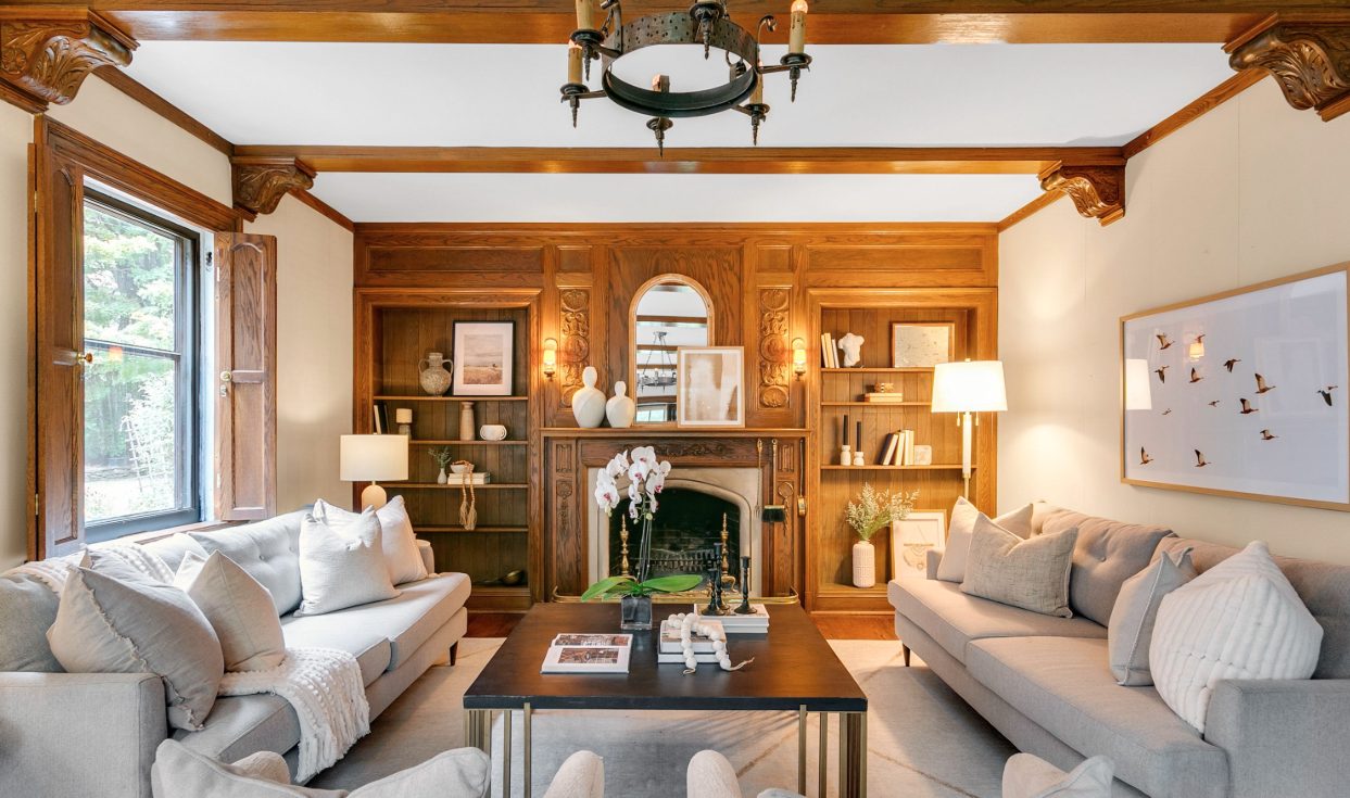 Living room with oak-panelled fireplace wall, carved corbels, built-in shelves and pale linen sofas